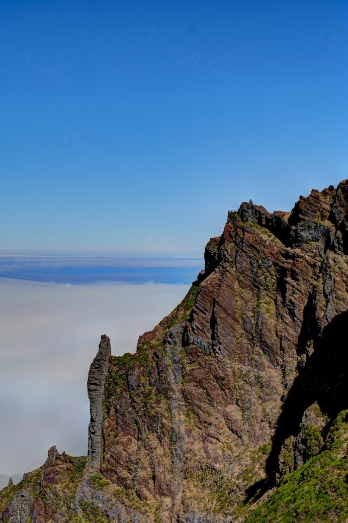 Punta rocciosa che emerge sopra una distesa di nuvole con cielo azzurro